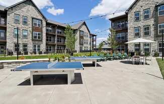 two ping pong tables in a courtyard with apartments in the background at The Depot Raymore, MO 64083