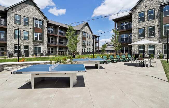 two ping pong tables in a courtyard with apartments in the background at The Depot Raymore, MO 64083