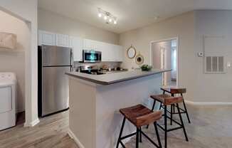 a kitchen with a breakfast bar and stools next to a washer and dryer at Autumn Park Apartments, Charlotte, 28262