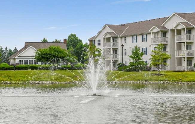 a fountain in the pond with an apartment building in the background