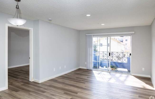 A room with a wooden floor and a sliding glass door leading to a balcony.