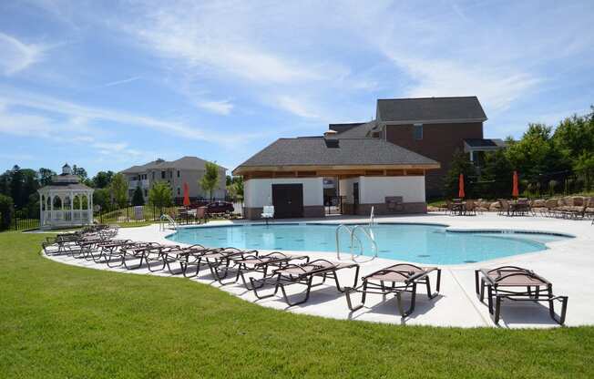 A beautiful resort-style pool, surrounded by lounge chairs, lush grass, a large sundeck, and a gazebo at Claremont on the Square.