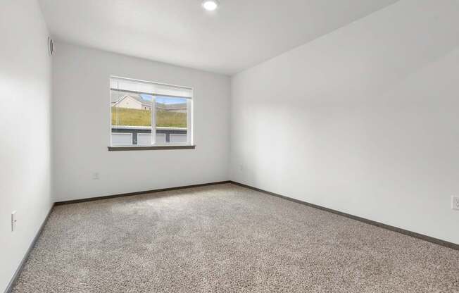 A room with a carpeted floor and a window showing a house and a fence outside.