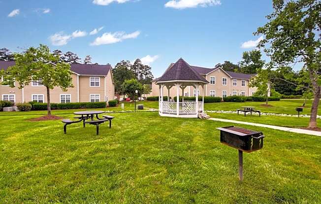 a gazebo and picnic tables in a grassy area with apartment buildings in the