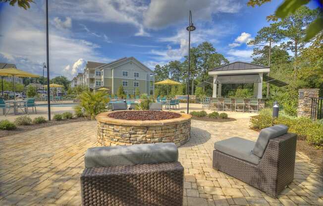 Poolside fire pit with oversized chairs, outdoor grilling station, and tables at Lullwater at Blair Stone apartments for rent in Tallahassee, FL