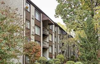 A building with a brown and beige exterior is surrounded by trees and bushes.