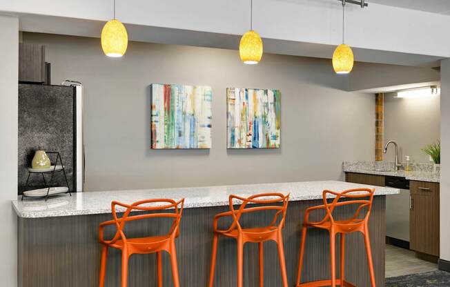 A kitchen with a bar area featuring orange chairs and a white counter.