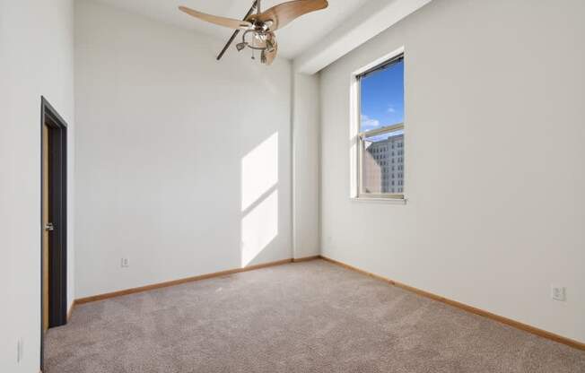 an empty bedroom with a ceiling fan and a window
