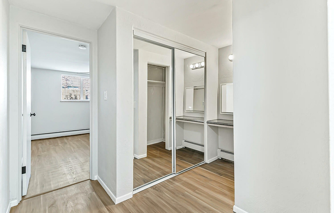 Elegant apartment hallway with mirrored closet doors, sleek wooden floors, and bright natural light.