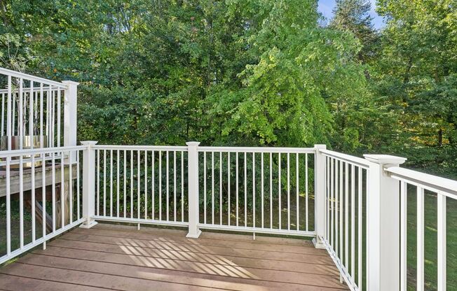 a deck with white railing and trees in the background