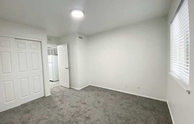 Bedroom with large sliding door closet, oversized window with white blinds on right, and door to hallway in back left corner at Summit, Pocatello, ID 83201