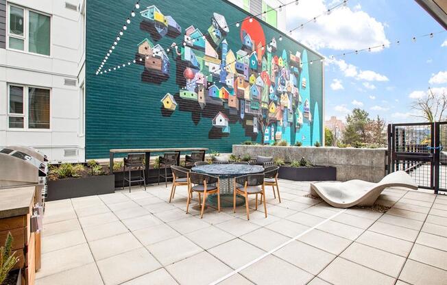 a patio with a table and chairs and a mural on the side of a building