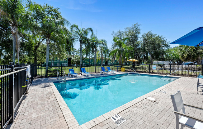 Inviting outdoor pool area with sun loungers and lush palm trees under a clear blue sky, offering a perfect relaxation spot.