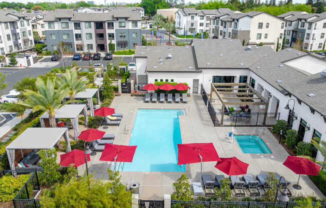 A pool surrounded by red umbrellas and lounge chairs.