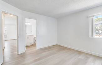A room with white walls and wooden flooring, with a window showing a building outside.