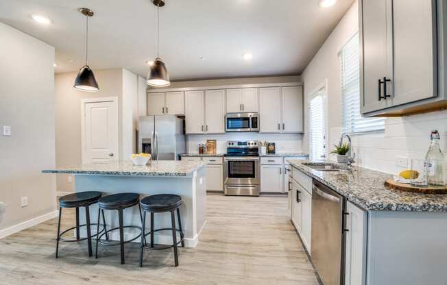Large kitchen with island and pendant lights above. Faux wood flooring throughout, with beautiful white cabinets and light countertops. Canvas at Denton spacious kitchen with ample natural lighting and large island, build to rent, homes for rent in Denton, professionally managed rental home community, private yards, low maintenance, pet-friendly.