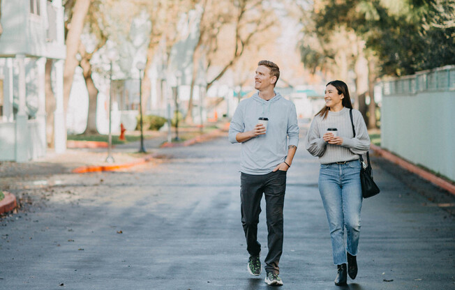 A young man and young woman walking together holding coffee