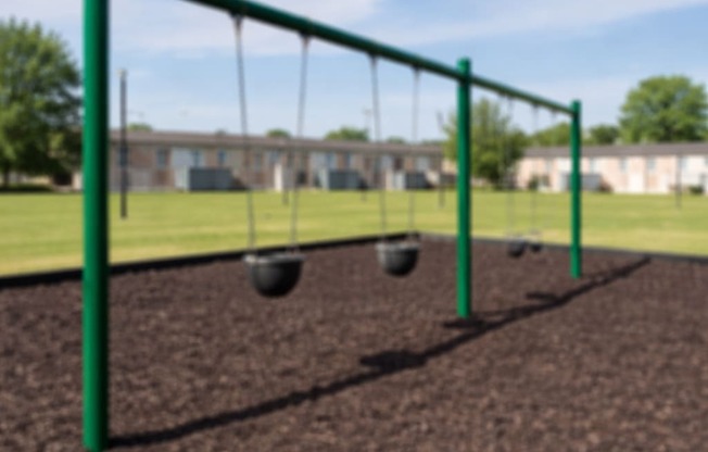 A swing set with two swings is in the foreground of a grassy area.