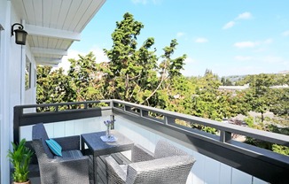 A balcony with a table and chairs overlooking a lush green landscape.