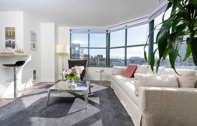 A living room with a white couch, a glass coffee table, and a large window.