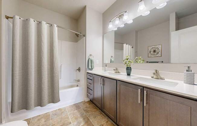 A bathroom with a shower curtain, two sinks, and a large mirror.