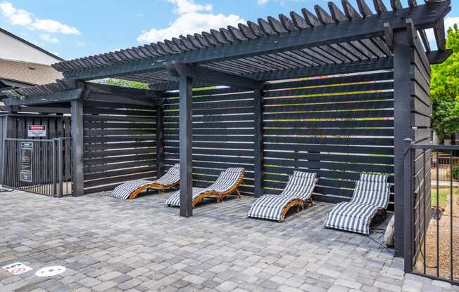 a pergola with chaise lounges on a brick patio