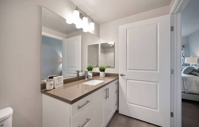 A bathroom with a white door and a mirror above the sink.