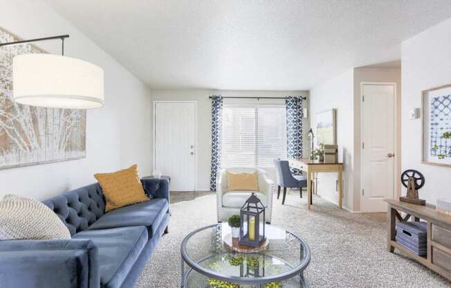 A living room with a blue couch and a glass coffee table.