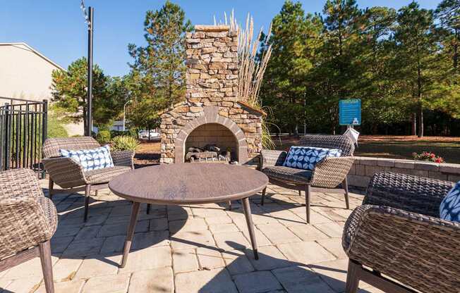 A patio with a stone fireplace and wicker chairs.