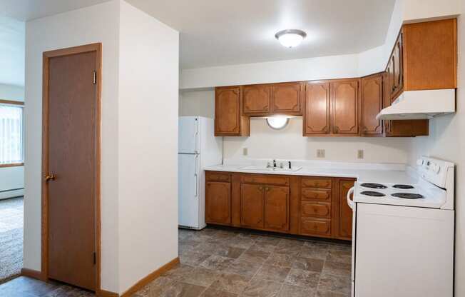 an empty kitchen with white appliances and wooden cabinets