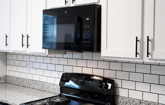A black microwave is mounted above a black stove in a kitchen.