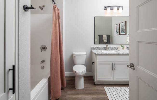 A bathroom with a toilet, sink, and a pink towel hanging on the shower rod.
