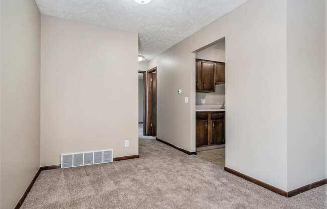 Omaha, NE Maple Ridge Apartments. A living room with a carpeted floor and a kitchen in the background