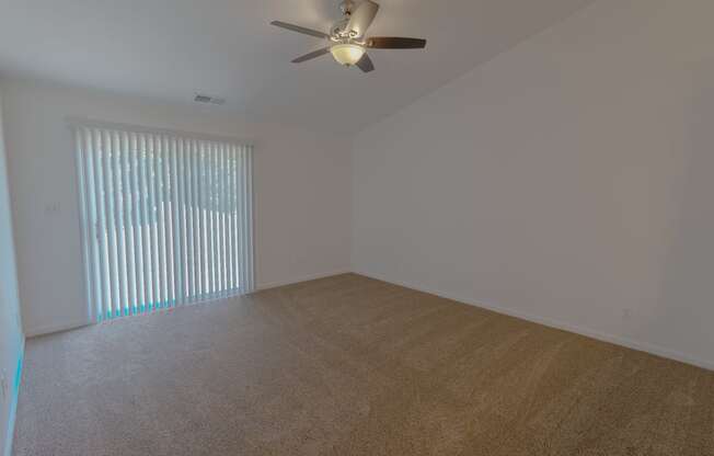 an empty living room with a large window and a ceiling fan