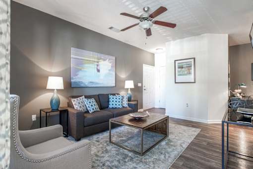 A living room with a brown couch, a grey armchair, a coffee table, and a ceiling fan.