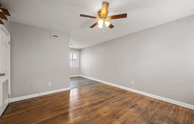 an empty living room with a ceiling fan and wood floors