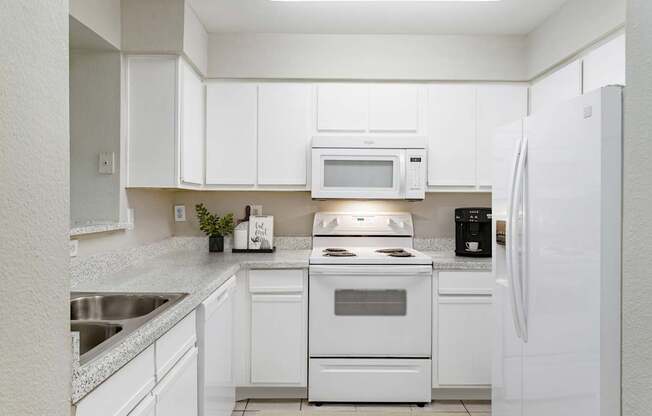 A white kitchen with a sink, stove, and refrigerator.