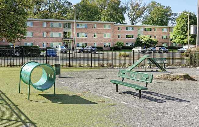 A dog park with a green slide and bench in front of a brick building.