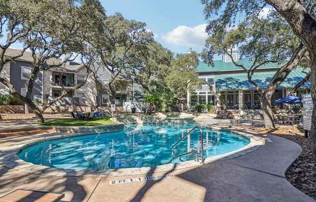 A swimming pool surrounded by trees and a building in the background.