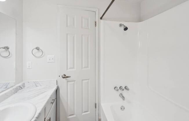 A white bathroom with a white tub and a white door.