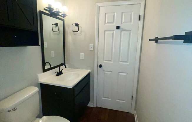 A white toilet sits in a small bathroom with a black cabinet and a white door.