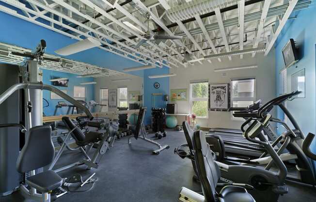 a gym with various exercise equipment in a building with blue walls at Village Club of Rochester Hills, Shelby Township, MI