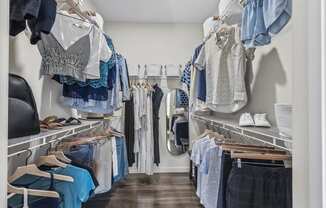 A walk in closet with clothes hanging on shelves and hangers.