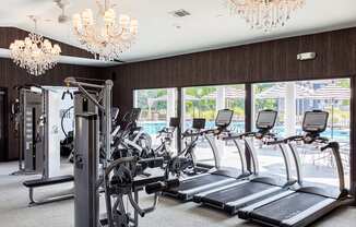 a room with a row of treadmills and two chandeliers hanging from the ceiling