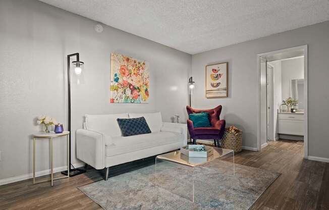 A living room with a white couch, a chair, and a painting on the wall.