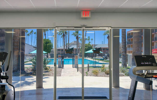 a view of a swimming pool from a gym with glass doors at Presidio Palms Apartments, Tucson, AZ