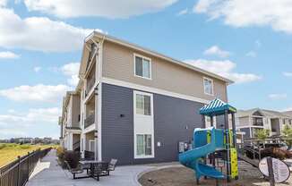 A playground area is in front of a two-story apartment building. at Connect at First Creek Apartments, Denver, CO