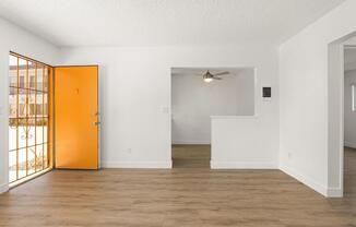 A room with a wooden floor and white walls, with a ceiling fan and a door leading to a balcony.