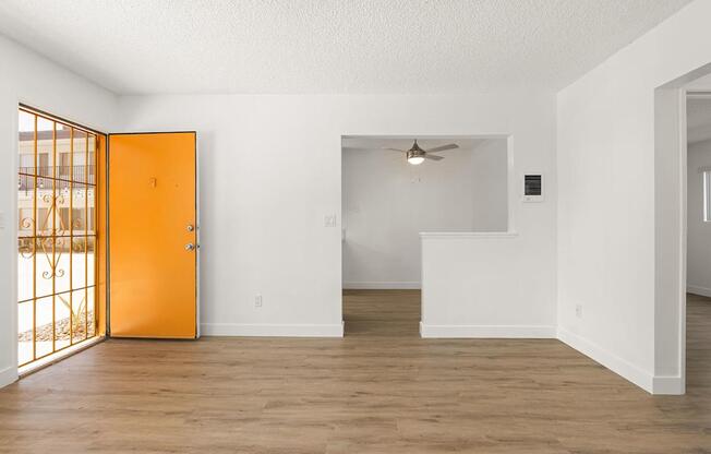 A room with a wooden floor and white walls, with a ceiling fan and a door leading to a balcony.