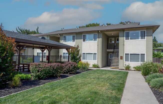 View of well landscaped courtyard with exterior building and gated community pool with covered area that has picnic table and seating